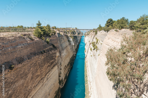 Seascape of both sides of Corinth's canal coast, left seaside glows in a golden sunrise light, right is in shadow, bridge contour and blue skies on background, noisy blurred water reflcetion