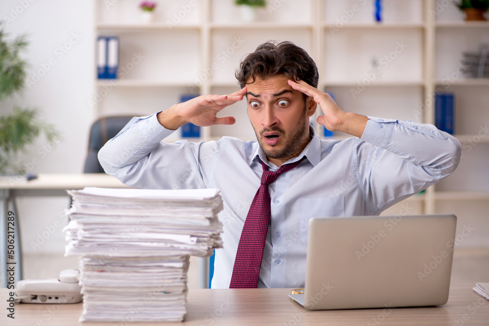 Young male employee and too much work in the office Young male employee and too much work in the office