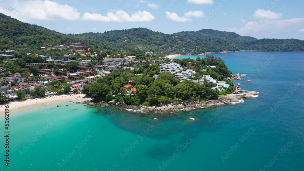 Clear water with a rocky Kata beach. The bottom is visible. Aerial view of the ocean and shore from the drone. The whole island is green. There are beautiful hotels. A tourist place in Thailand