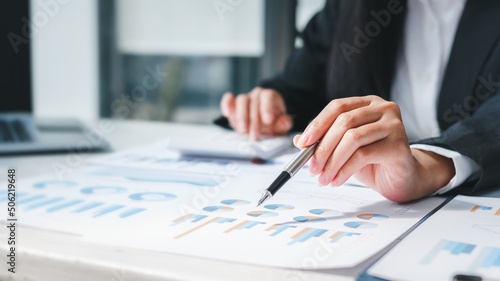 Close up businesswoman's hands holding pen and using calculator placed on messy office .