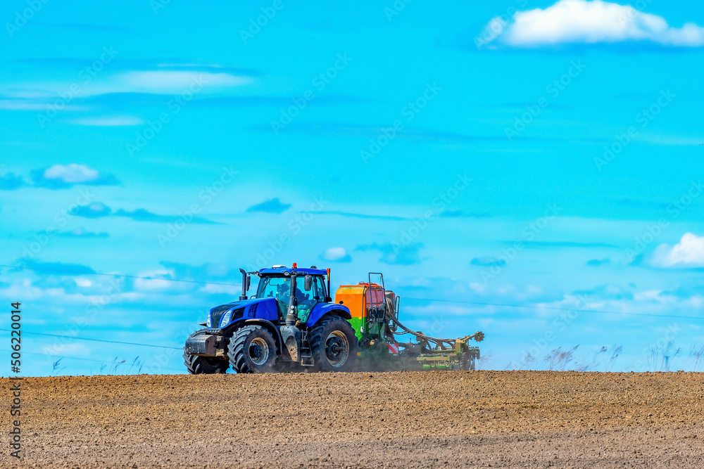 Obraz premium A tractor with a seeder sows grains of wheat or oats in the spring in a field for growing grain products against a sky with clouds.