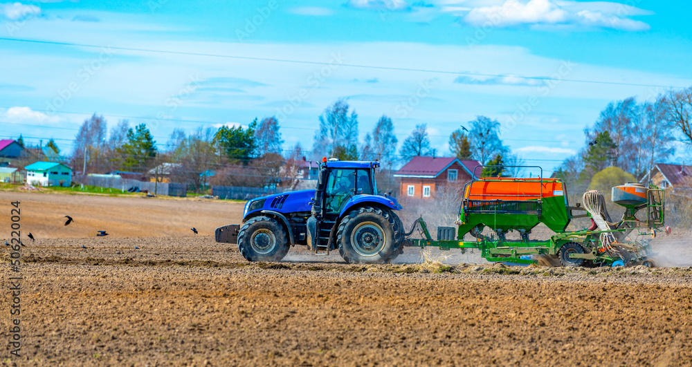 Obraz premium Mozhayskoe, Russia, 06 May 2022, A tractor with a seeder in the field sows grains of wheat or oats to grow grain products.