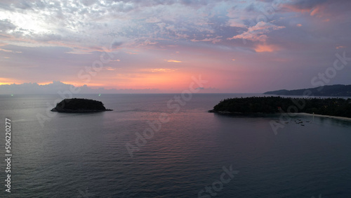 The red-orange sunset is reflected with clouds in the sea. An island can be seen in the distance. Smooth water is like a mirror. There is a lonely island. Not far from the shore of the boat. Epic