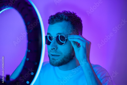 Man shots a video on a phone with a ring lamp, portrait video blogger streaming in glasses neon light photo