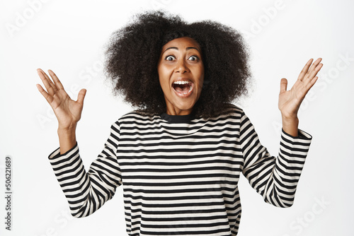 Enthusiastic african american woman celebrating, scream yes, looking amazed and surprised, winning, triumphing over success, standing against white background