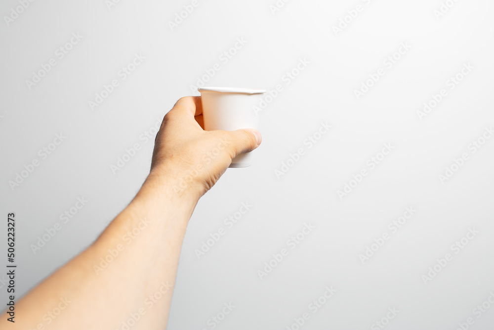 Close-up of male hand holding white paper cup of coffee takeaway, on grey. Close-up of male hand holding white paper cup of coffee takeaway, on grey.