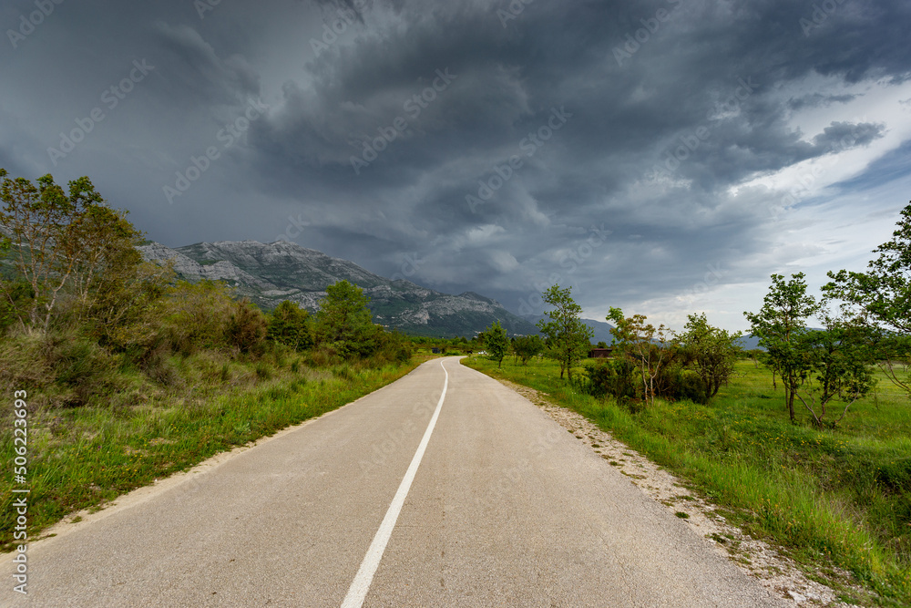 Empty countryside road in valley. Landscape with dramatic sky. A storm is coming from the mountains.