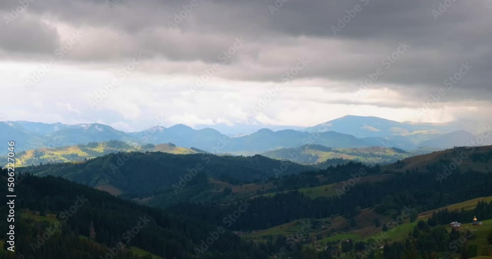 View of the mountains, a large gray cloud hangs in the sky, creating a shadow over the green forest hills. Spring summer in the Carpathians, Ukraine. View of the mountains, a large gray cloud hangs in the sky, creating a shadow over the green forest hills. Spring summer in the Carpathians, Ukraine.