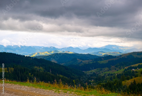 View of the mountains, a large gray cloud hangs in the sky, creating a shadow over the green forest hills. Spring summer in the Carpathians, Ukraine.