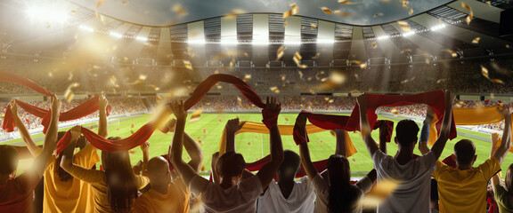 Back view of football, soccer fans cheering their team with scarfs at crowded stadium at game time. Concept of sport, support, competition. Out of focus effect