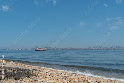 The rocky beach of Kinaliada Island with a ship sailing on the Sea of Marmara in the background and the city of Istanbul in the distance, Turkey photo