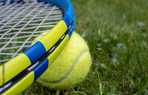 Close up selected focus of high tech lightweight tennis racquet frame with synthetic gut strings and tennis ball on a grass court