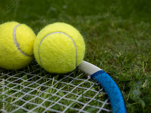 Close up selected focus of Carbon fibre lightweight tennis racquet gut strings and tennis balls on a grass court