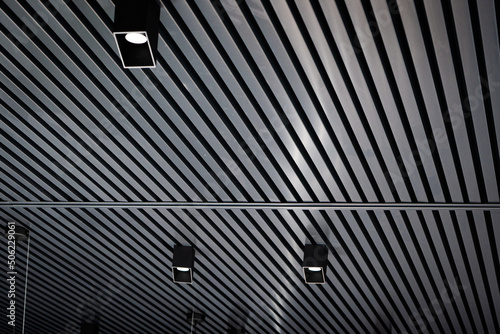 Bottom view of lath ceiling with spot lights. Abstract modern architecture or interior background in black and white with geometric structure.