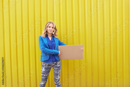 Beautiful blonde woman on yellow background holding a cardboard sign