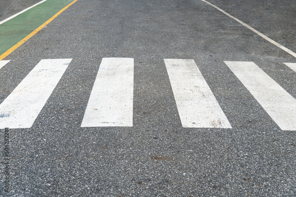 White road crosswalk or crossing path on asphalt road. The pedestrian control path is painted green beside of the road. White road crosswalk or crossing path on asphalt road. The pedestrian control path is painted green beside of the road.