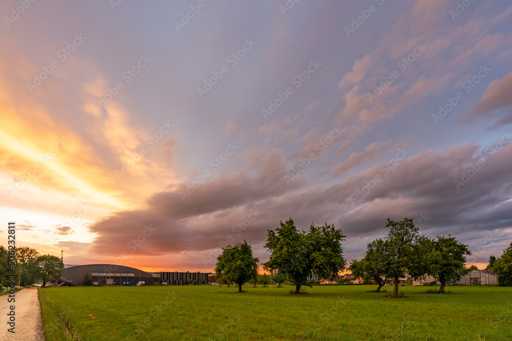 Abendrot nach abziehendem Gewitter. dramatischer Sonnenuntergang im Rheintal mit grüne Wiesen, Bäumen und farbige und graue Wolken, Dornbirn, Vorarlberg, Austria