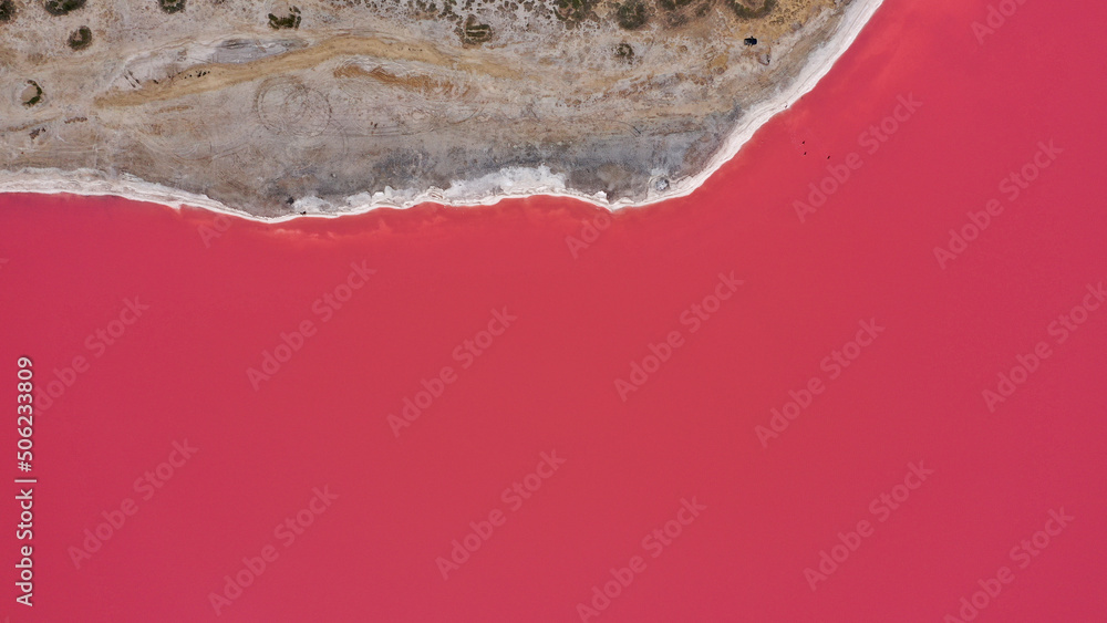 Flying over a pink salt lake. Salt production facilities saline evaporation pond fields in the salty lake. Dunaliella salina impart a red, pink water in mineral lake with dry cristallized salty coast.