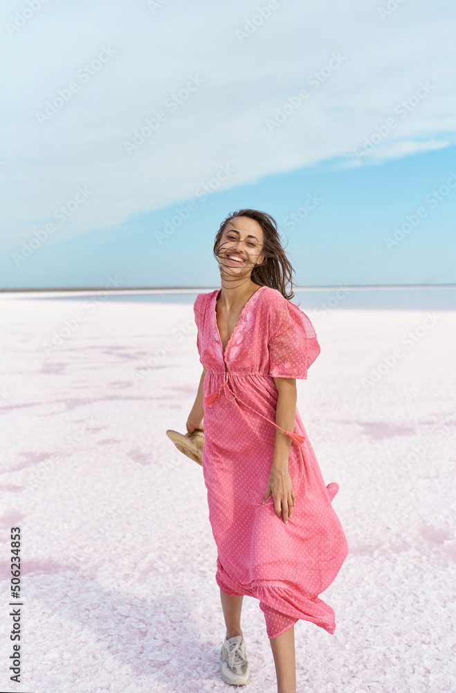 Full hight portrait of happy emotionally woman with blowing hair wearing pink dress, walking by windy salt paradise beach of pink lake Full hight portrait of happy emotionally woman with blowing hair wearing pink dress, walking by windy salt paradise beach of pink lake