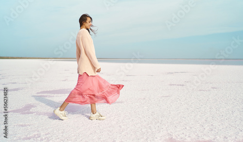 Foto Cheerful walking woman in oversize sweater and blowing pink dress at paradise white coast of pink lake