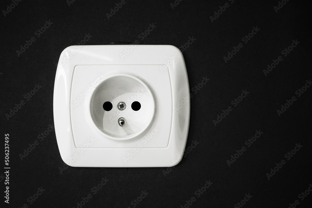 Electrical socket isolated on black wall. Renovated studio apartment power supply background. Empty copy space single white plastic power outlet. Electrical socket isolated on black wall. Renovated studio apartment power supply background. Empty copy space single white plastic power outlet.