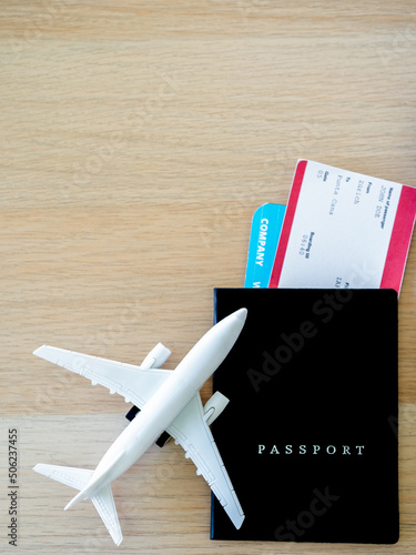 Passport black cover with flight ticket near white airplane toy on wooden desk with copy space, top view, vertical style. Online ticket booking for travel concept.