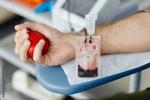 Close up of male hand squeezing stress ball while donating blood at medical volunteer center focus on blood bag in foreground  copy space