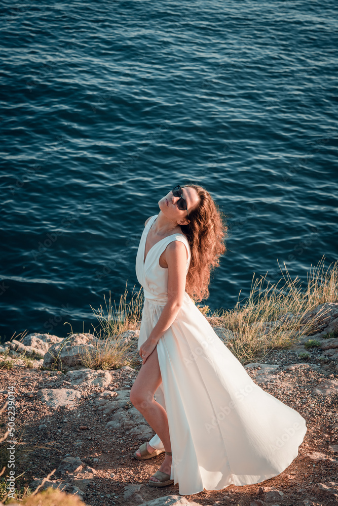 Stylish bride standing back with wedding bouquet on beautiful landscape of sea and mountains on sunset