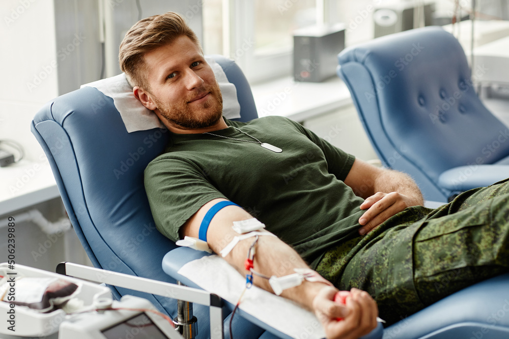 Portrait of smiling young man giving blood at donor center in comfort while lying in chair, copy space - obrazy, fototapety, plakaty 