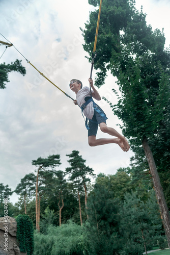 Boy bungee jumping in trampoline. Teenager in an amusement park is having fun. Vertical frame.
