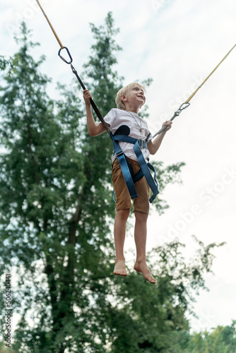 Blond boy jumping on trampoline in an amusement park. Child frolics and jumps high. Vertical frame.