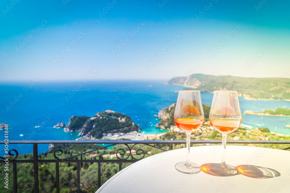Two glasses of white wine with Corfu in background - obrazy, fototapety, plakaty 