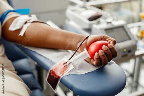 Closeup of black woman donating blood focus on hand holding red ball with tubing, copy space