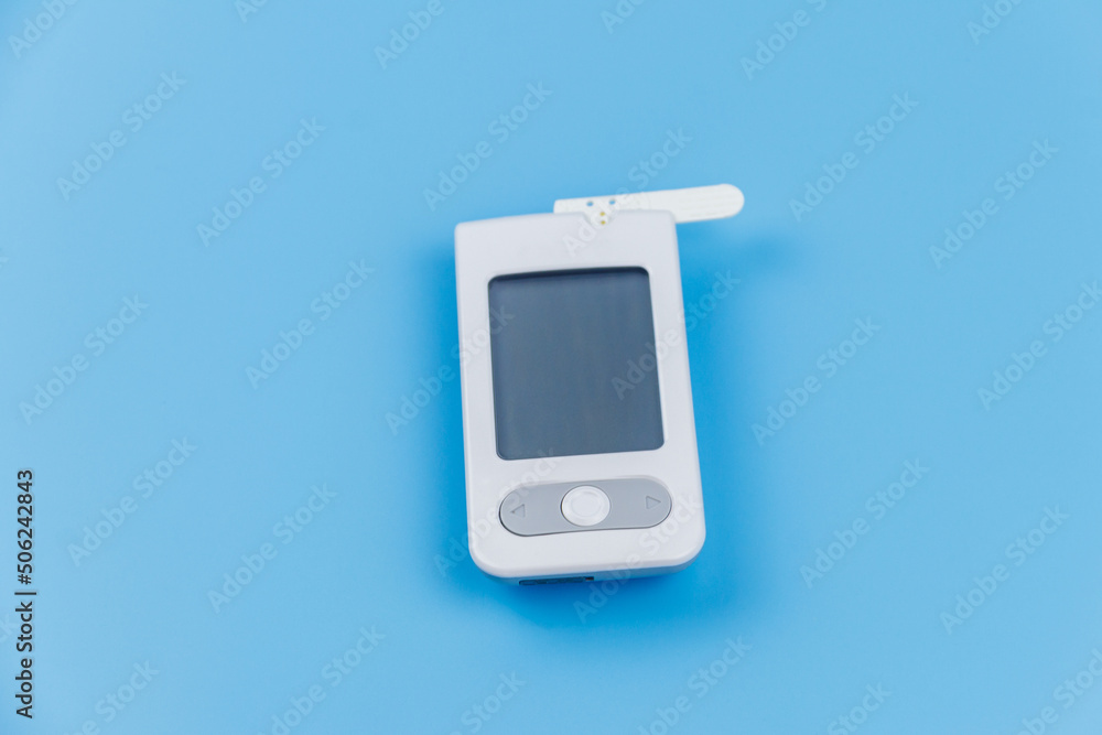 Digital glucometer with test strip on a pastel blue background. Diabetes concept Digital glucometer with test strip on a pastel blue background. Diabetes concept