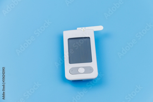 Digital glucometer with test strip on a pastel blue background. Diabetes concept