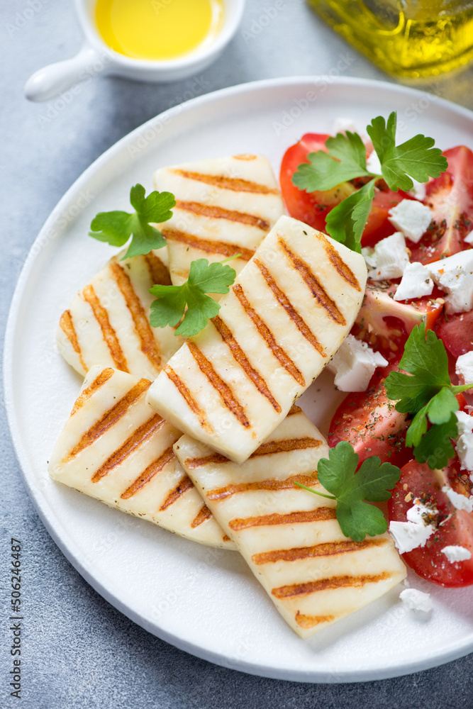 White plate with slices of grilled halloumi cheese, tomatoes and fresh parsley, vertical shot, selective focus, close-up White plate with slices of grilled halloumi cheese, tomatoes and fresh parsley, vertical shot, selective focus, close-up