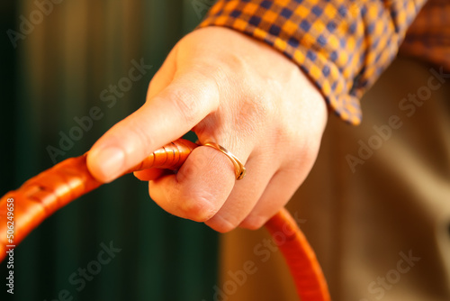 Defocus closeup female hand holding handle of wicker or wooden basket. Orange color. Minimal dark light steel background. Arch design. Reed straw. Out of focus