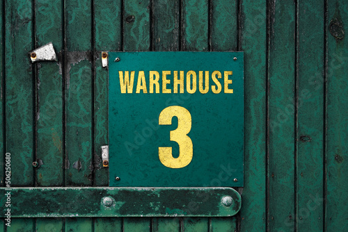 Green sign "Warehouse 3" on an old warehouse door in a whisky distillery