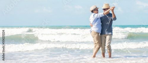 Asian senior couple wearing hat with sunglasses  holding hands dancing  on the beach