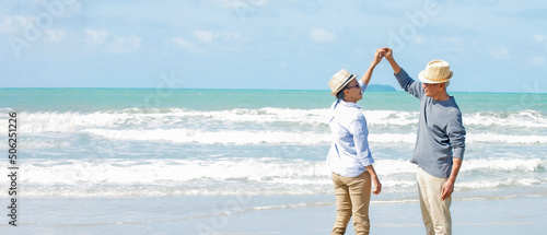 Asian senior couple wearing hat with sunglasses  holding hands dancing  on the beach