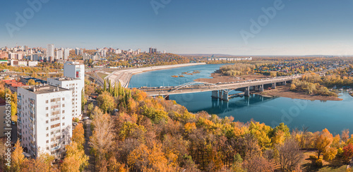 Aerial cityscape view of city districts with automobile bridge over river in Ufa. Autumn parks with colorful trees