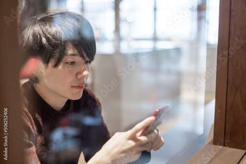 カフェの窓辺でスマートフォンを操作する20代男性