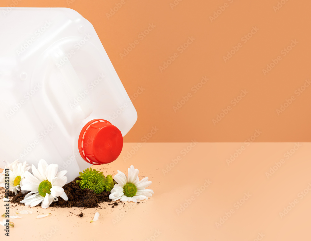 Negative impact on nature. Plastic canister crushes beautiful flowers on an orange background. The concept of environmental damage. The idea of plastic pollution and soil pollution. Copy space