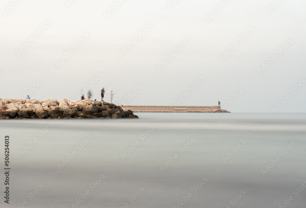Long exposure to sea water with the port and a dyke with fishermen in the background.
