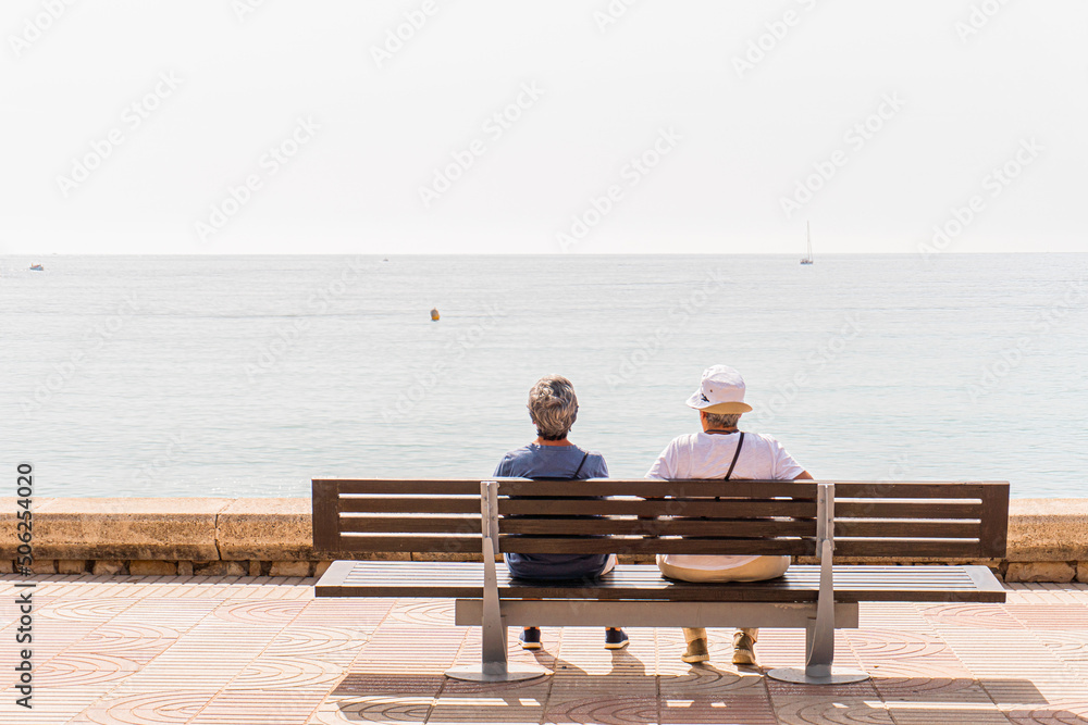 Unrecognizable man and woman sitting on a bench enjoying the sea view on a sunny summer day. Unrecognizable man and woman sitting on a bench enjoying the sea view on a sunny summer day.