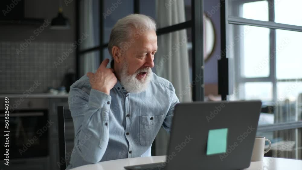Sick elderly 60s bearded male communicating with general practitioner, receiving online consultation using video conference on laptop, sitting at table in modern living room. Shooting in slow motion. Sick elderly 60s bearded male communicating with general practitioner, receiving online consultation using video conference on laptop, sitting at table in modern living room. Shooting in slow motion.