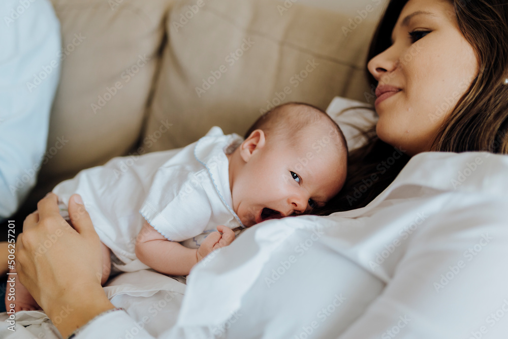 Happy newborn baby boy yawning on top of his mother lying on the sofa Happy newborn baby boy yawning on top of his mother lying on the sofa