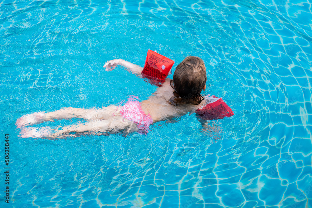 A little girl is swimming in the pool in inflatable armbands. A child in the pool. Safety on the water. Summer children's holidays