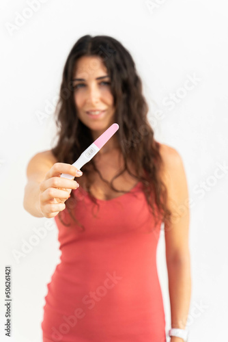 a pregnant brunette woman showing a pregnancy test in a white background. She is pregnant and showing the pregnancy test. 