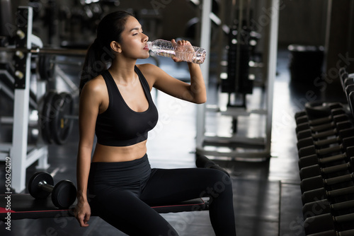 Fit Asian woman drink water after dumbbell exercise in fitness gym